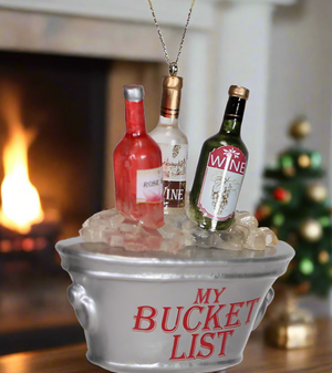 The Canton Christmas Shop Wine Bucket List Glass Ornament in front of a christmas tree and fire