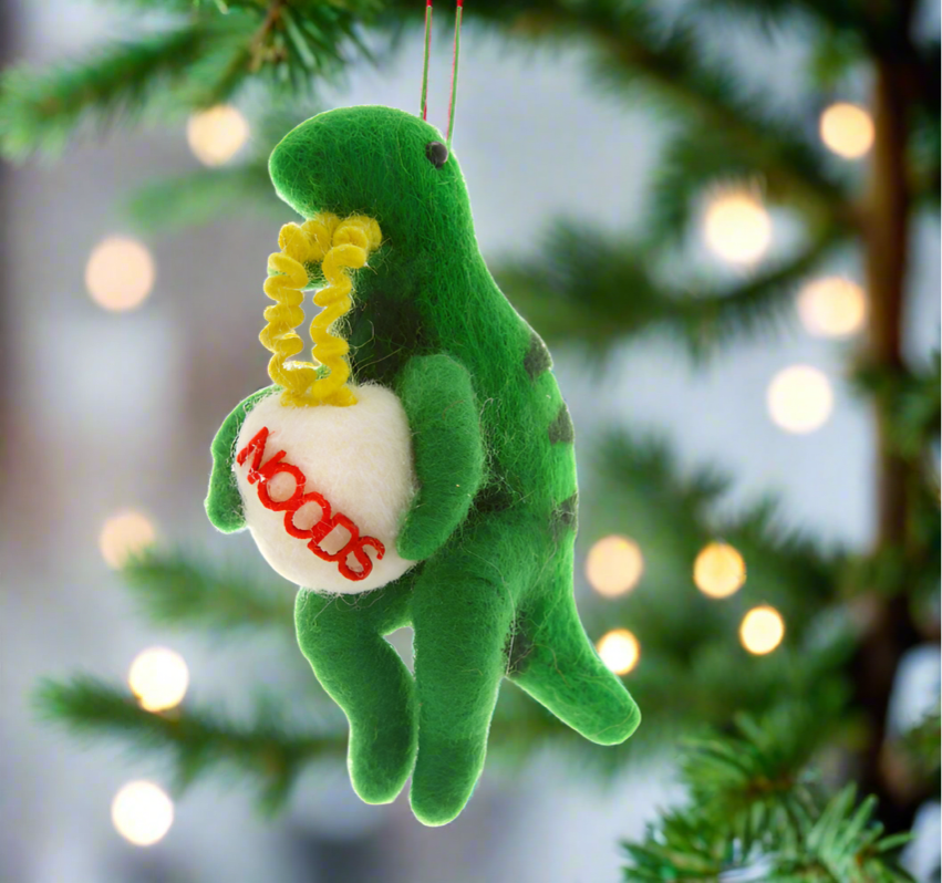 The Canton Christmas Shop Cody Foster Dinosaur with Ramen Noodles Soup Ornament in front of bowl of ramen