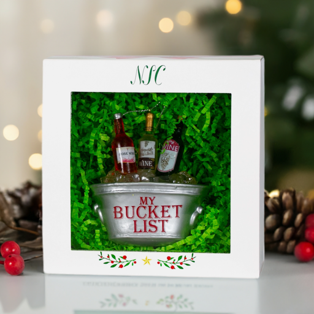 The Canton Christmas Shop Wine Bucket List Glass Ornament in front of a christmas tree and fire